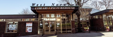 Photograph of the front entrance of West Norwood Library. Above the entrance is a decorative sign reading “West Norwood Library & Picturehouse.” Trees and a pavement are visible in front of the building.