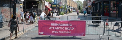 A picture of Atlantic Road, blocked off to cars, with a red sign, with white writing, that says Reimagining Atlantic Road, Open to People