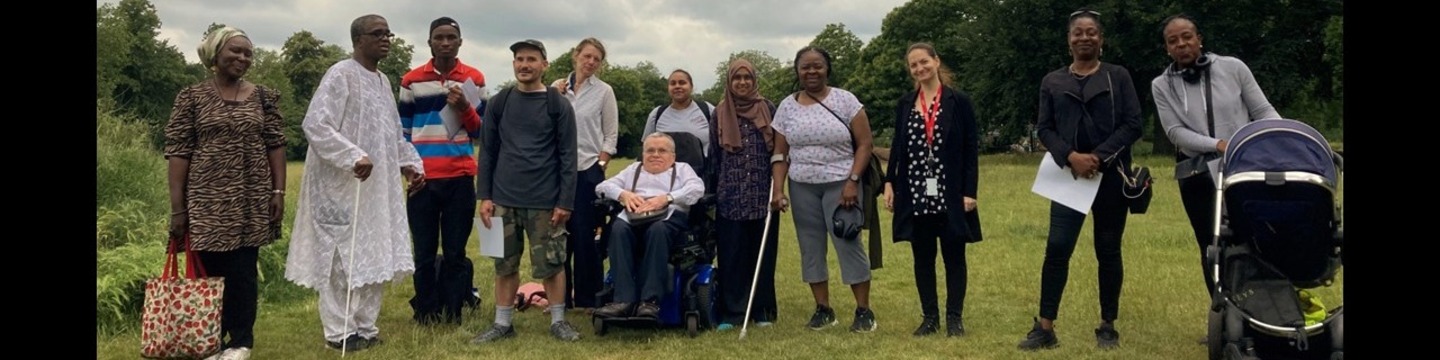 A group of diverse people in a Lambeth park.  Visible are some walking aids including a crutch, a white stick, a wheelchair, and a baby buggy..
