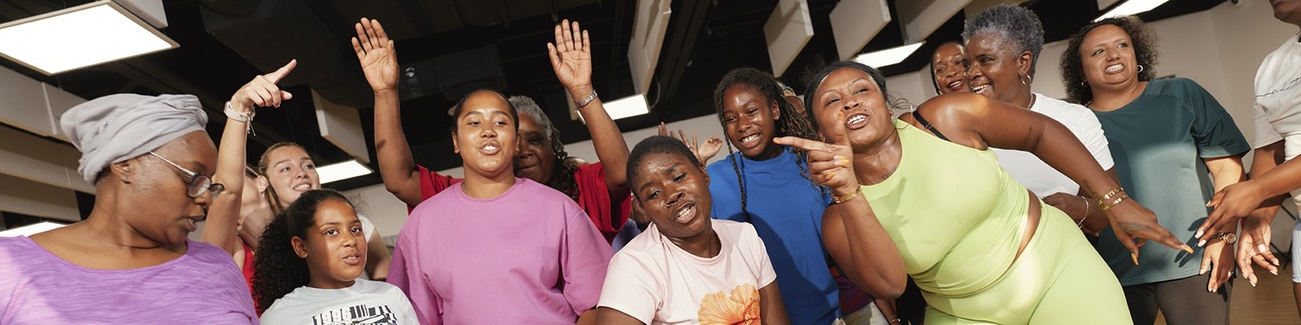 Twelve women and girls in sportswear, cropped, dancing close together.