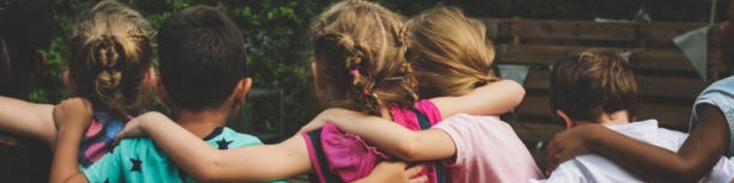 A group of children hugging each other facing away from the camera 